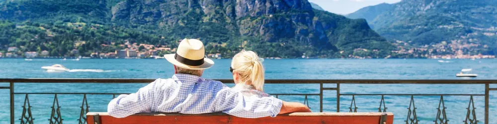 Senior couple sitting on bench enjoying a waterfront view in Italy